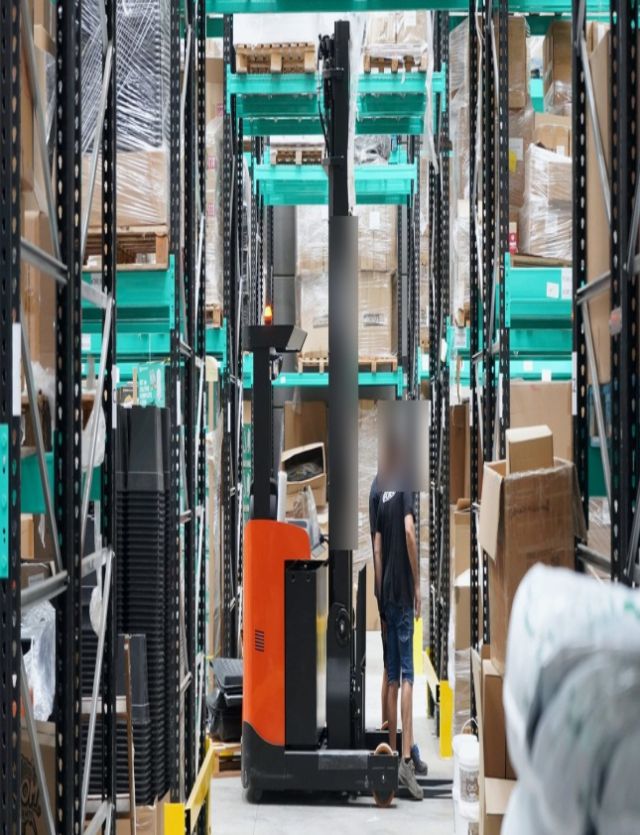 Organised industrial warehouse aisle with palletised materials and handling equipment.